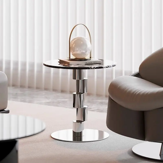 A modern round side table with a dark marble top and a polished chrome pedestal base.